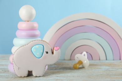 Photo of Tasty cookie in shape of cute elephant, pacifier and toys on light blue wooden table. Baby shower party