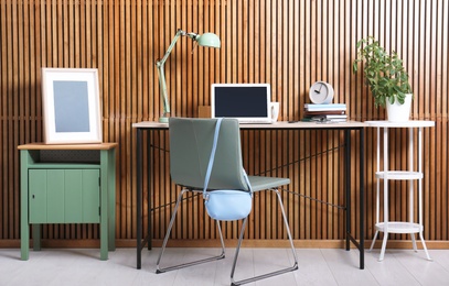 Stylish workplace interior with laptop on table near wooden wall. Space for text