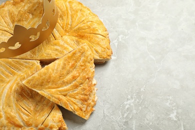 Traditional galette des Rois with paper crown on grey marble table, above view. Space for text