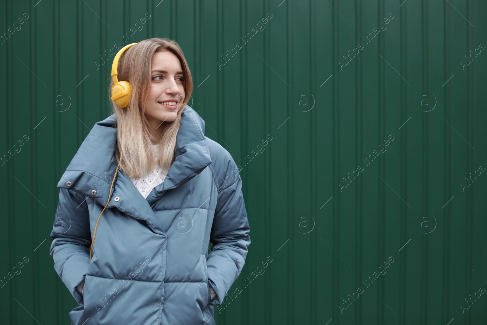 Photo of Young woman with headphones listening to music near color wall. Space for text