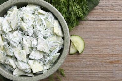 Photo of Delicious cucumber salad in bowl and ingredients on wooden table, flat lay. Space for text