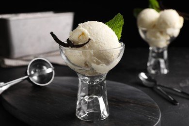 Photo of Tasty ice cream with vanilla pods in glass dessert bowl on black table