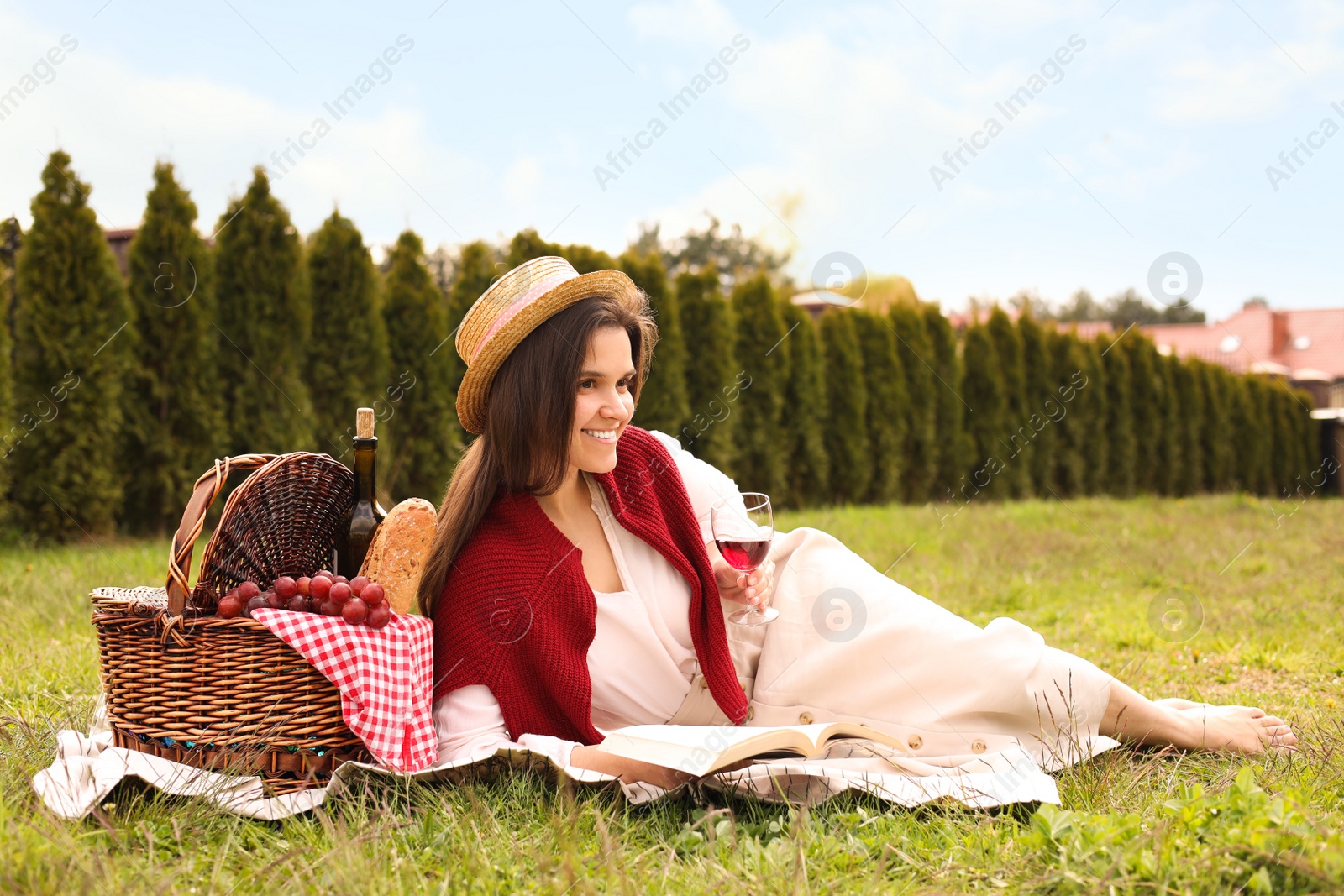 Photo of Happy woman with glass of wine reading book in park. Picnic season