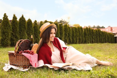 Happy woman with glass of wine reading book in park. Picnic season