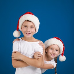 Image of Happy little children in Santa hats on blue background. Christmas celebration