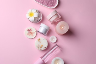 Photo of Different spa products, plumeria flower and burning candles on pink background, flat lay