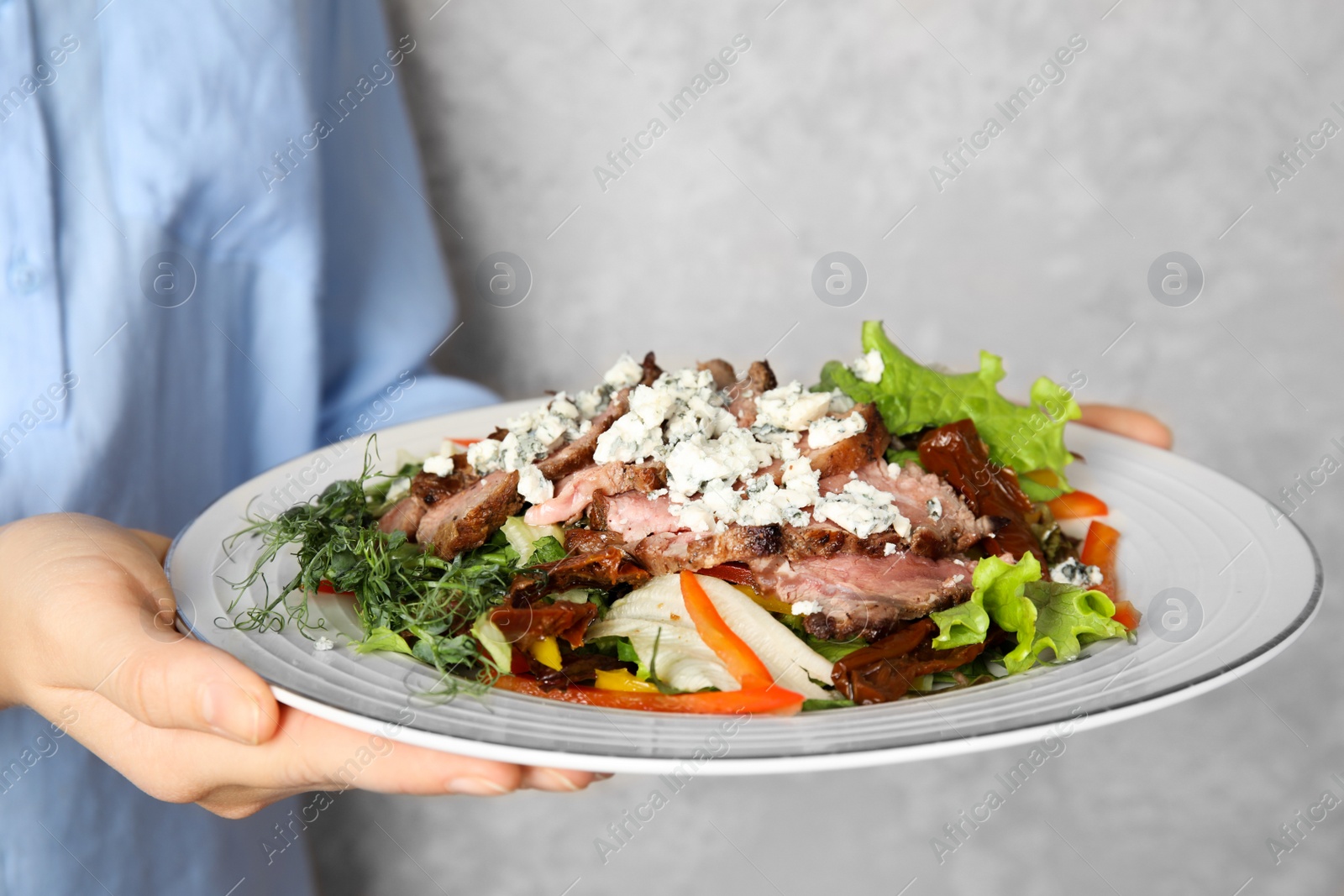 Photo of Woman holding plate with delicious salad on grey background, closeup