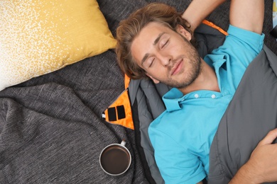 Young man in comfortable sleeping bag on blanket, top view