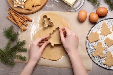 Photo of Woman making Christmas cookies with cutters at grey table, top view