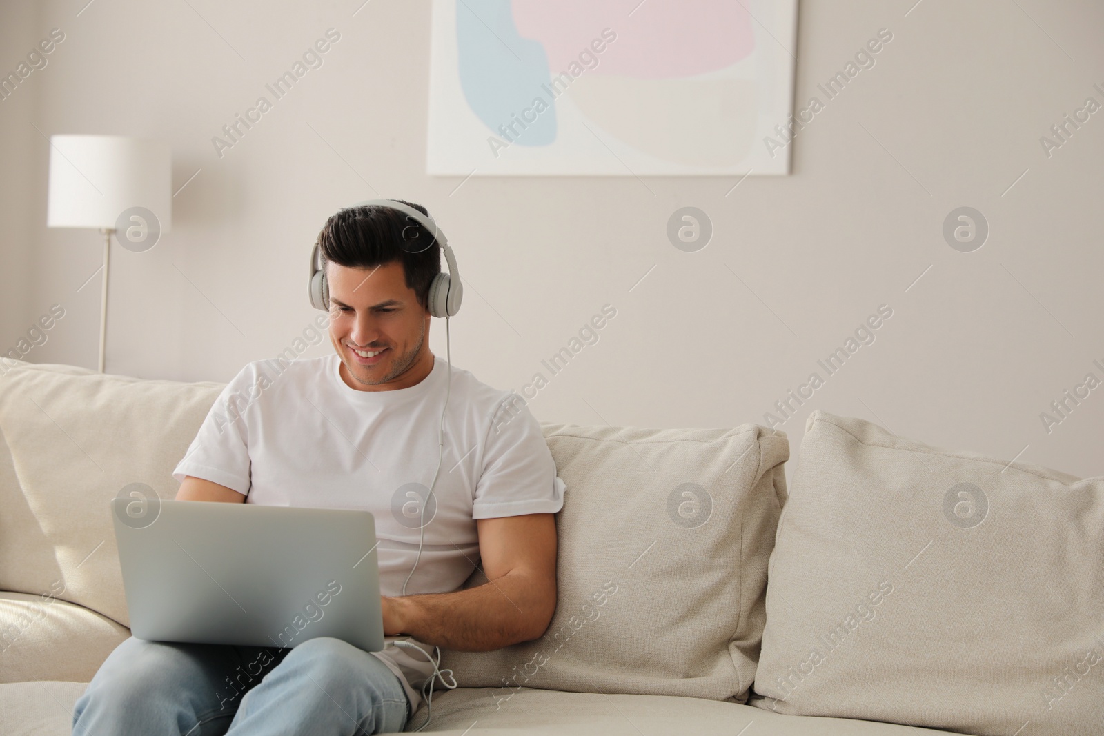 Photo of Man with laptop and headphones sitting on sofa at home