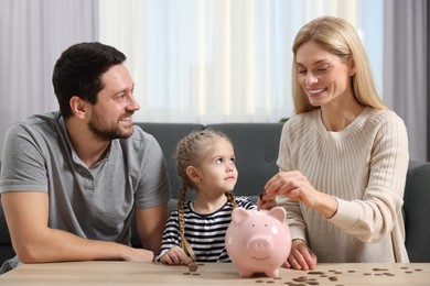 Family budget. Little girl and her parents putting coins into piggy bank at home