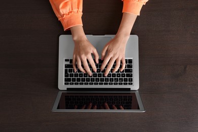 Photo of Woman working with laptop at wooden table, top view