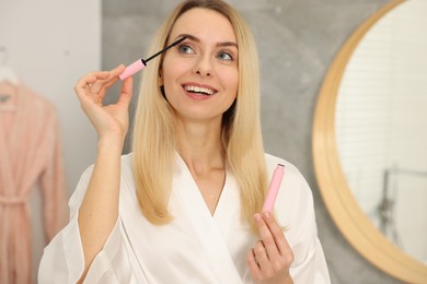 Photo of Beautiful happy woman applying mascara in bathroom