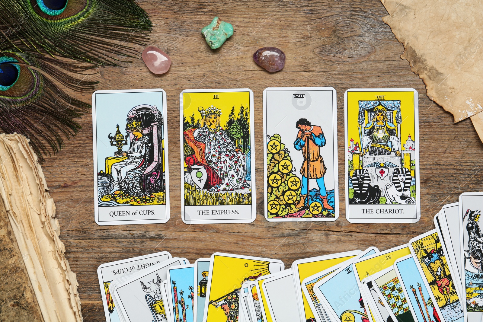 Photo of Tarot cards, old book, peacock feather and crystals on wooden table, flat lay