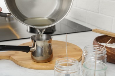 Photo of Pouring melted wax into cezve on table in kitchen. Making homemade candles