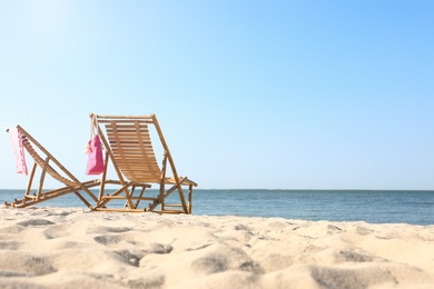 Empty wooden sunbeds and beach accessories on sandy shore