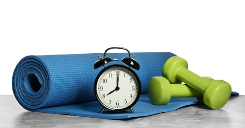 Alarm clock, yoga mat and dumbbells on marble table against grey background. Morning exercise