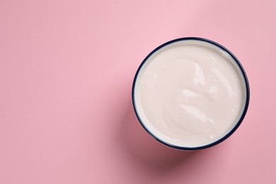 Photo of Bowl of tasty yogurt on pink background, top view. Space for text