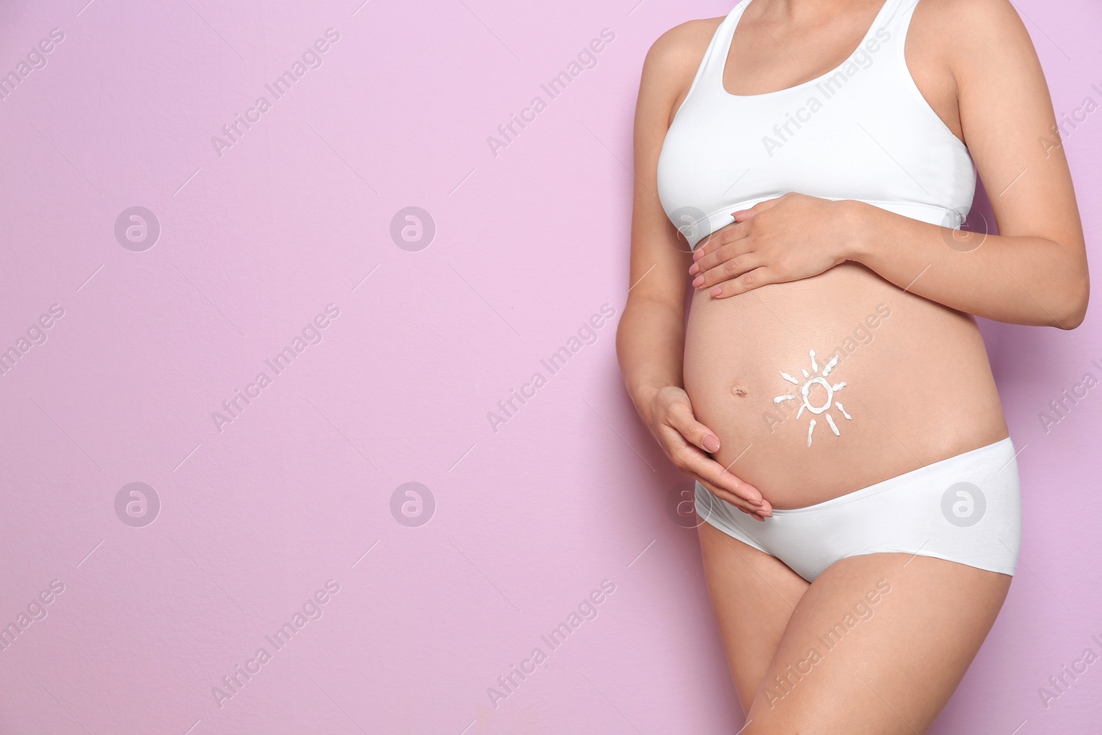 Photo of Sun painted with body cream on pregnant woman's belly against color background, closeup. Space for text