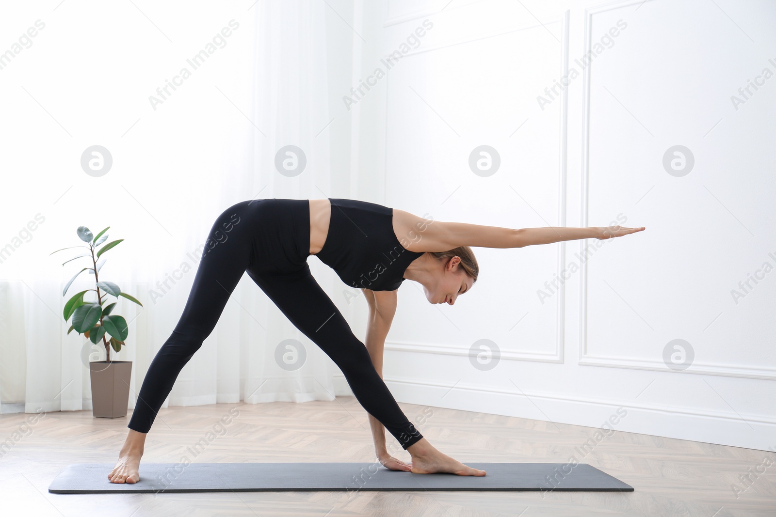 Photo of Young woman practicing triangle asana in yoga studio. Trikonasana pose