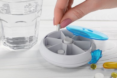 Photo of Woman putting pill into plastic box at white wooden table, closeup