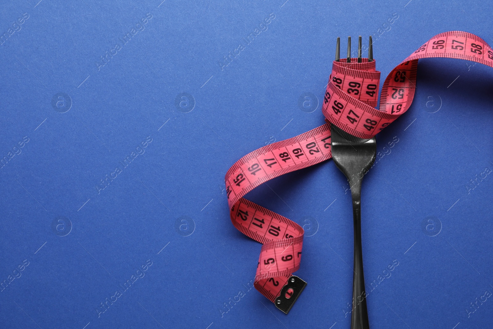 Photo of Fork with measuring tape on blue background, top view and space for text. Diet concept