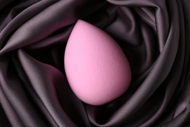 Pink makeup sponge on dark silk cloth, top view
