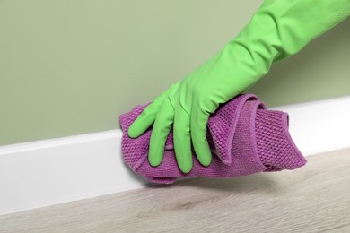 Photo of Woman in protective glove cleaning plinth with washcloth indoors, closeup