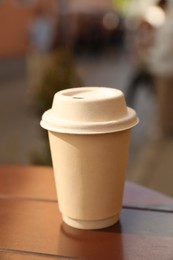 Photo of Cardboard takeaway coffee cup with lid on wooden table in city