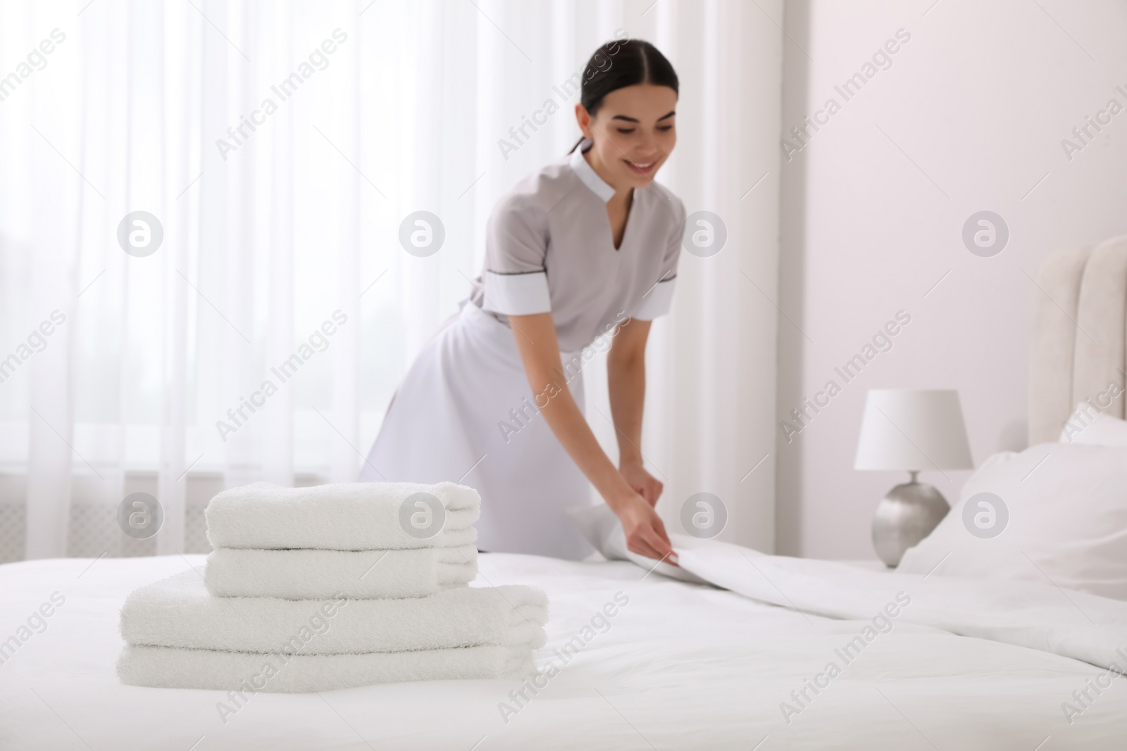 Photo of Chambermaid making bed in hotel room, focus on fresh towels. Space for text