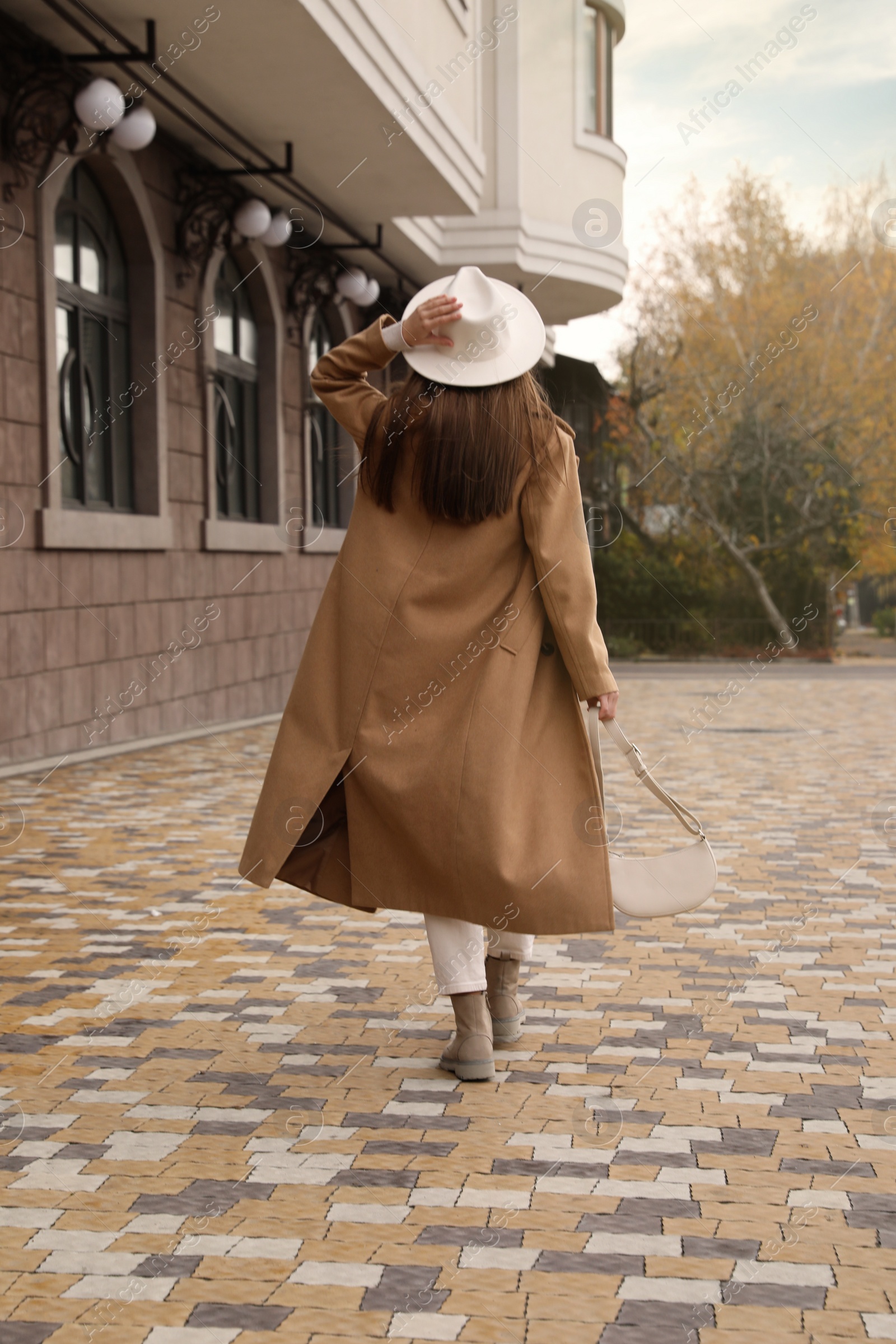 Photo of Young woman wearing stylish autumn clothes on city street, back view