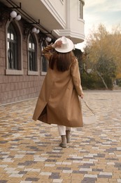 Photo of Young woman wearing stylish autumn clothes on city street, back view