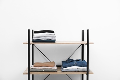 Photo of Modern shelves unit with stacked clothes near white wall