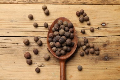 Aromatic allspice pepper grains in spoon on wooden table, top view