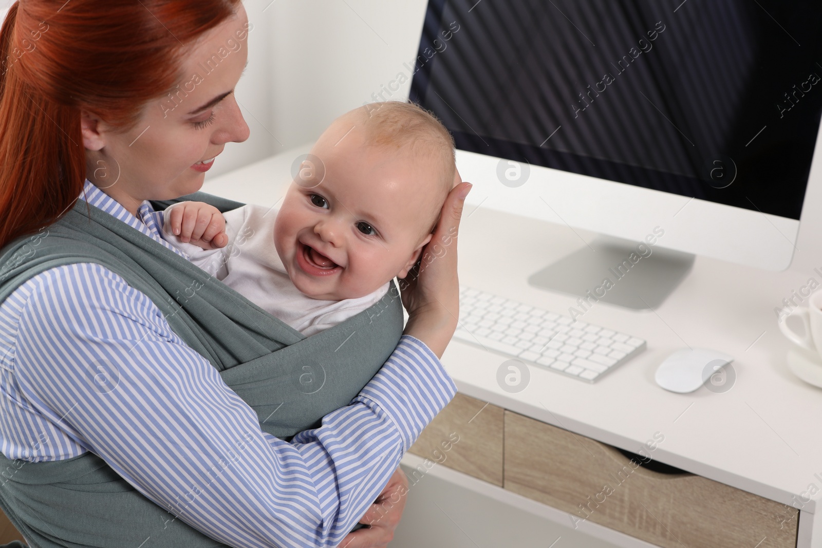 Photo of Mother holding her child in sling (baby carrier) at workplace