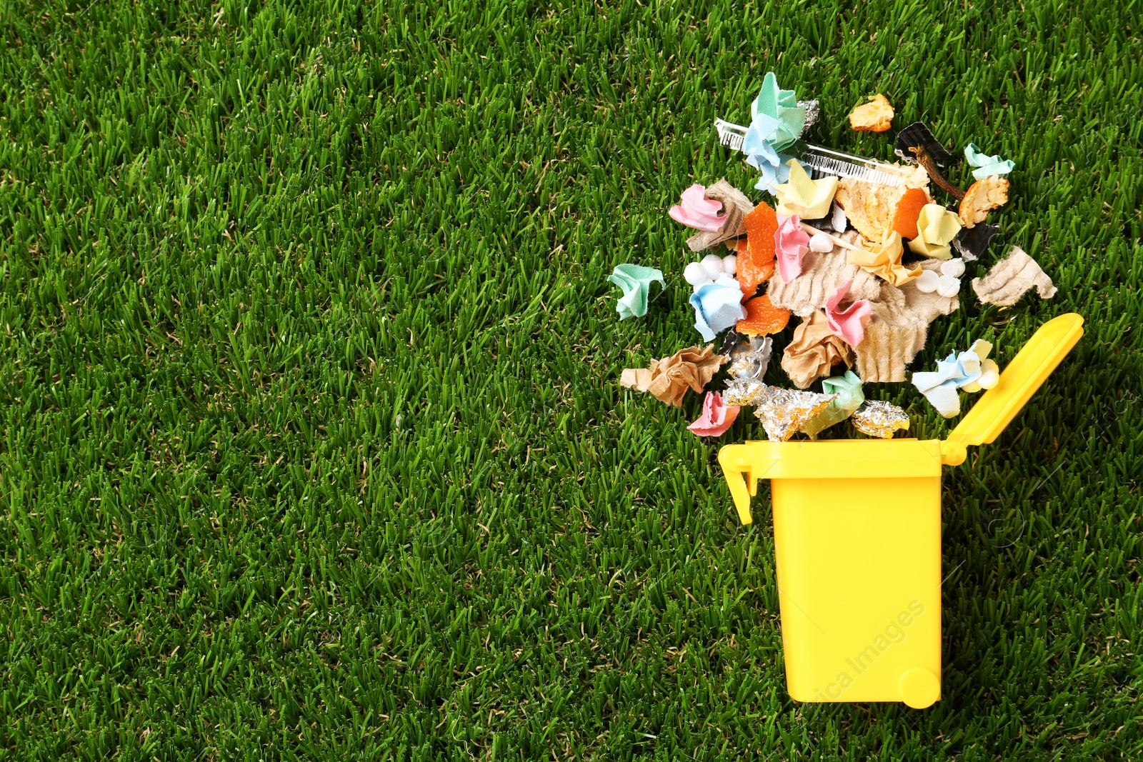 Photo of Trash bin and different garbage on green grass, top view with space for text. Waste recycling concept