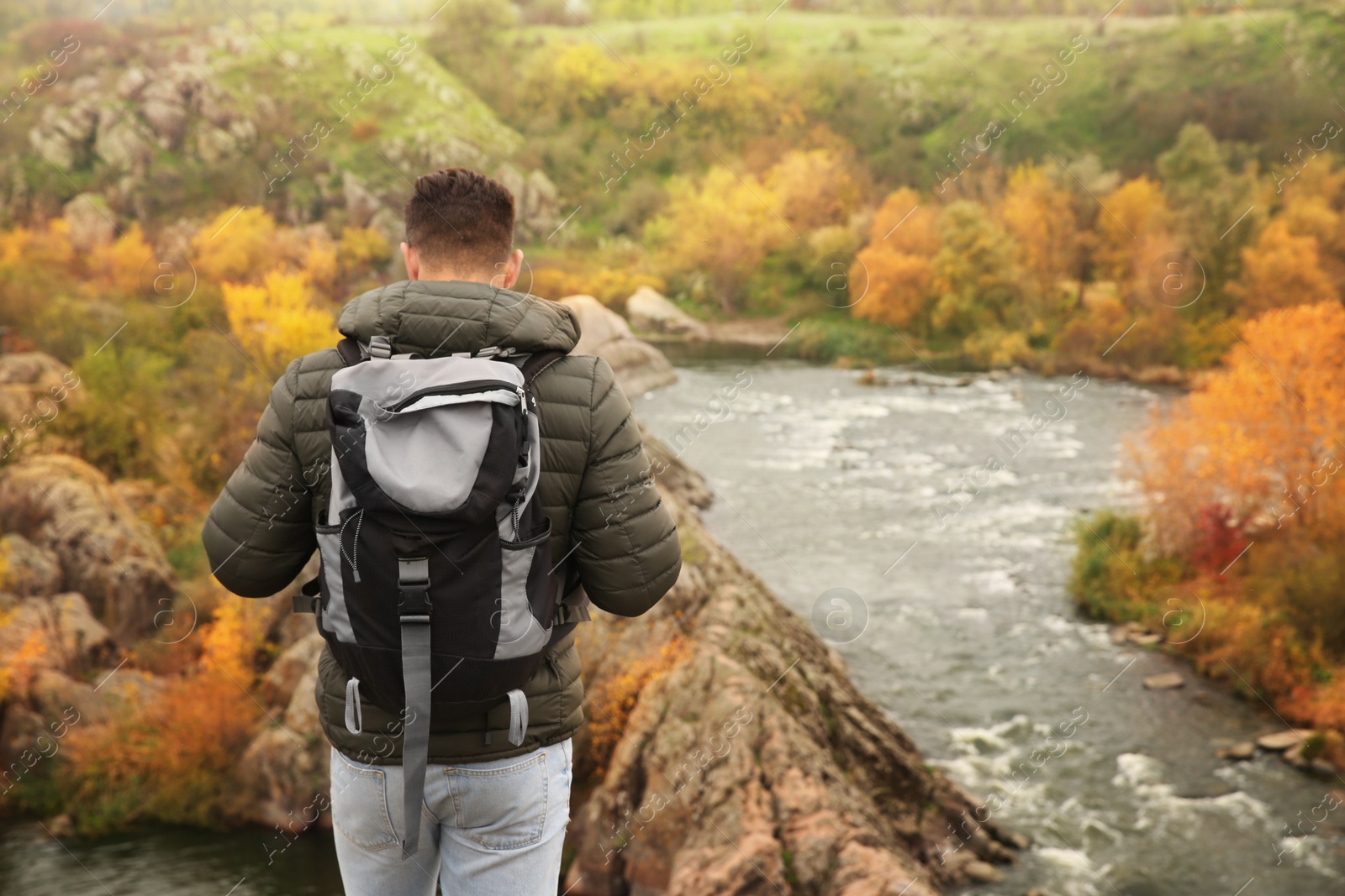 Photo of Man with travel backpack enjoying nature near mountain river, back view