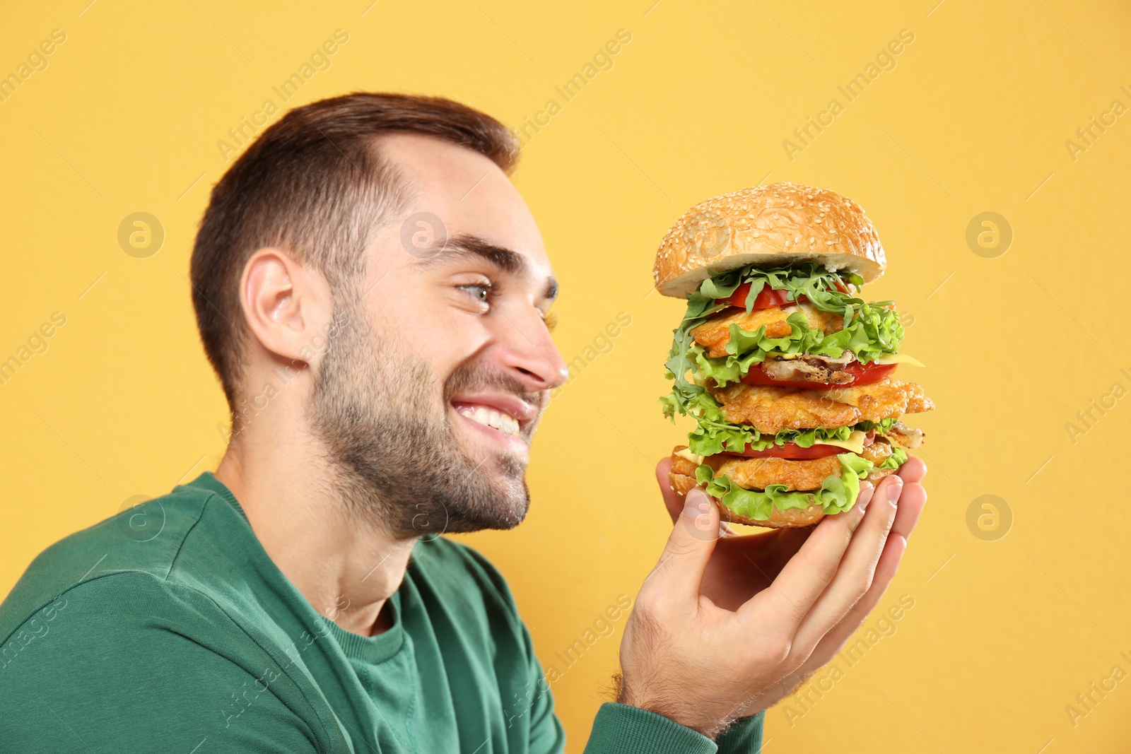 Photo of Young hungry man eating huge burger on color background