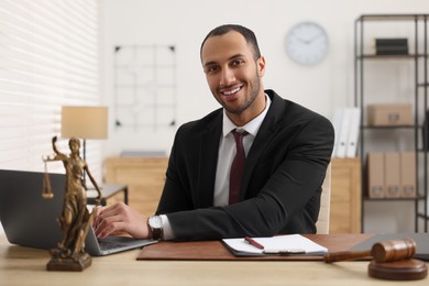 Photo of Smiling lawyer working with laptop at table in office