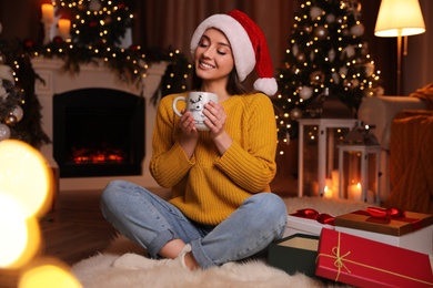 Beautiful young woman with cup of hot drink in living room decorated for Christmas