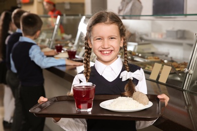 Photo of Cute girl holding tray with healthy food in school canteen