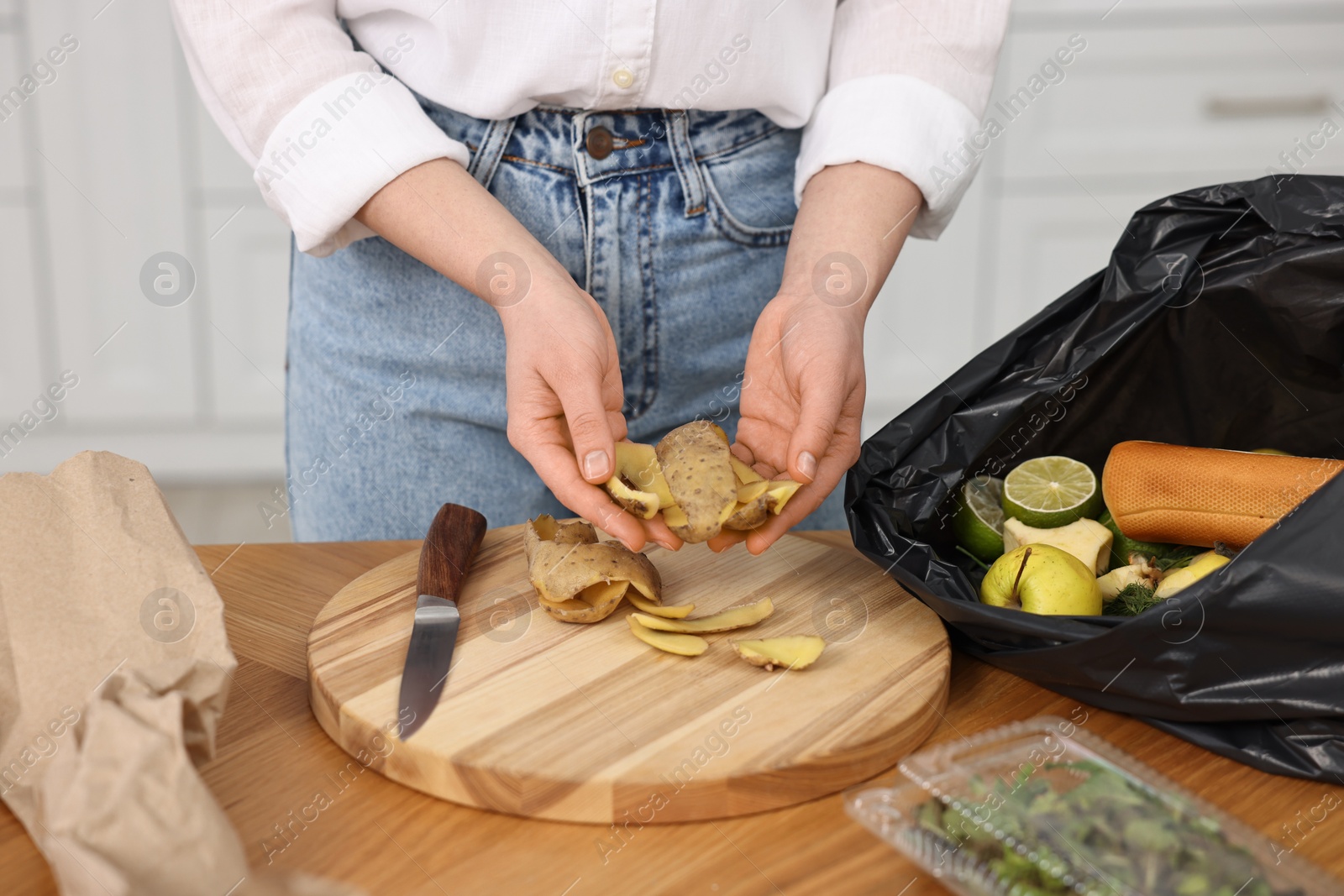 Photo of Garbage sorting. Woman putting food waste into plastic bag at wooden table indoors, closeup