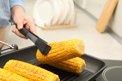 Photo of Woman taking corn from grill pan with tongs in kitchen, closeup