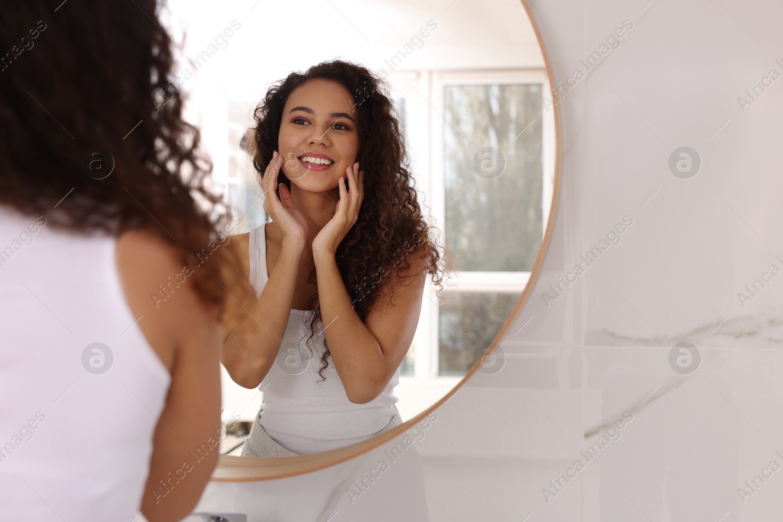 Photo of Beautiful African American woman near mirror in bathroom, space for text