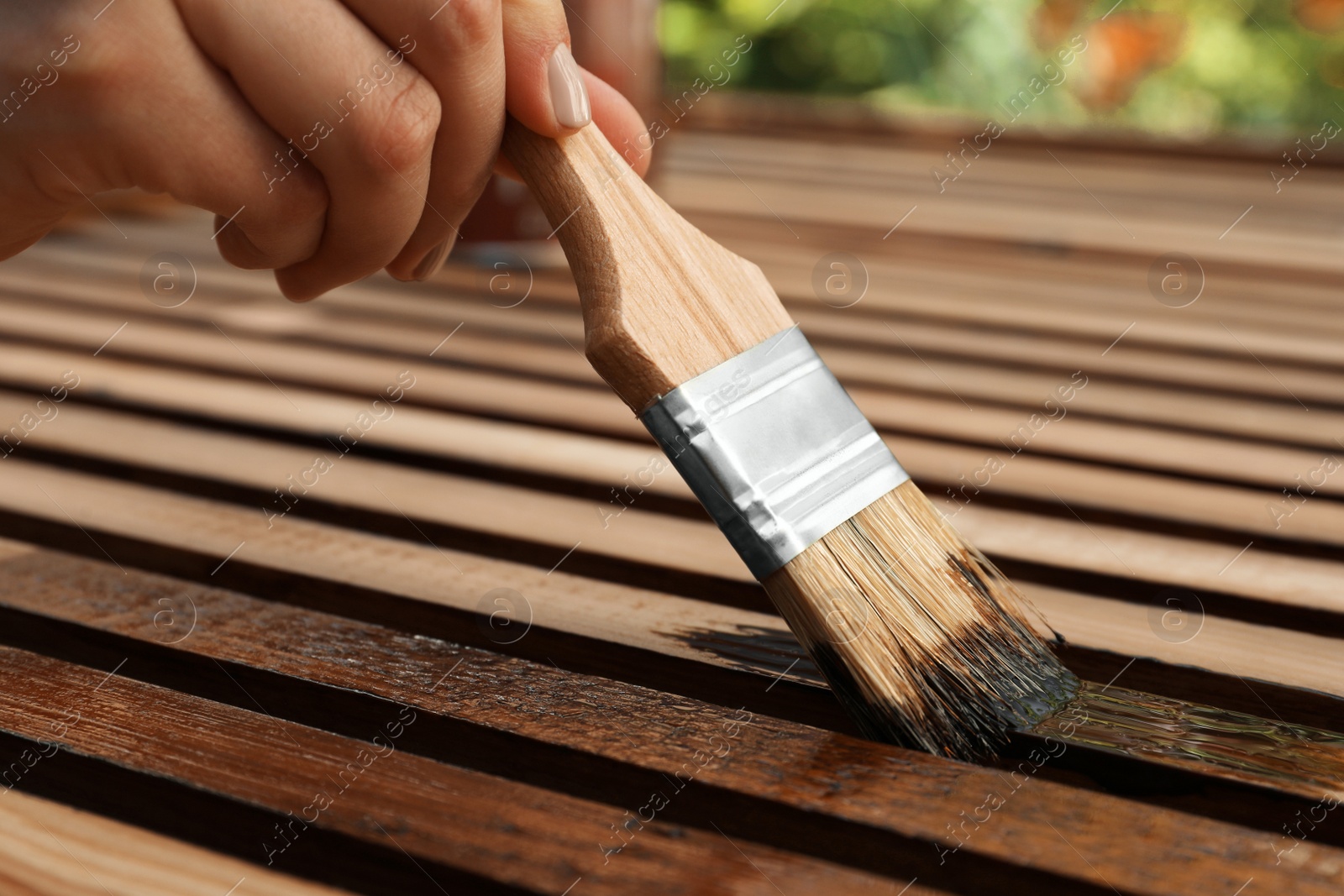 Photo of Woman applying wood stain onto planks outdoors, closeup