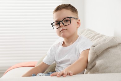 Photo of Cute little boy in glasses on sofa at home. Space for text