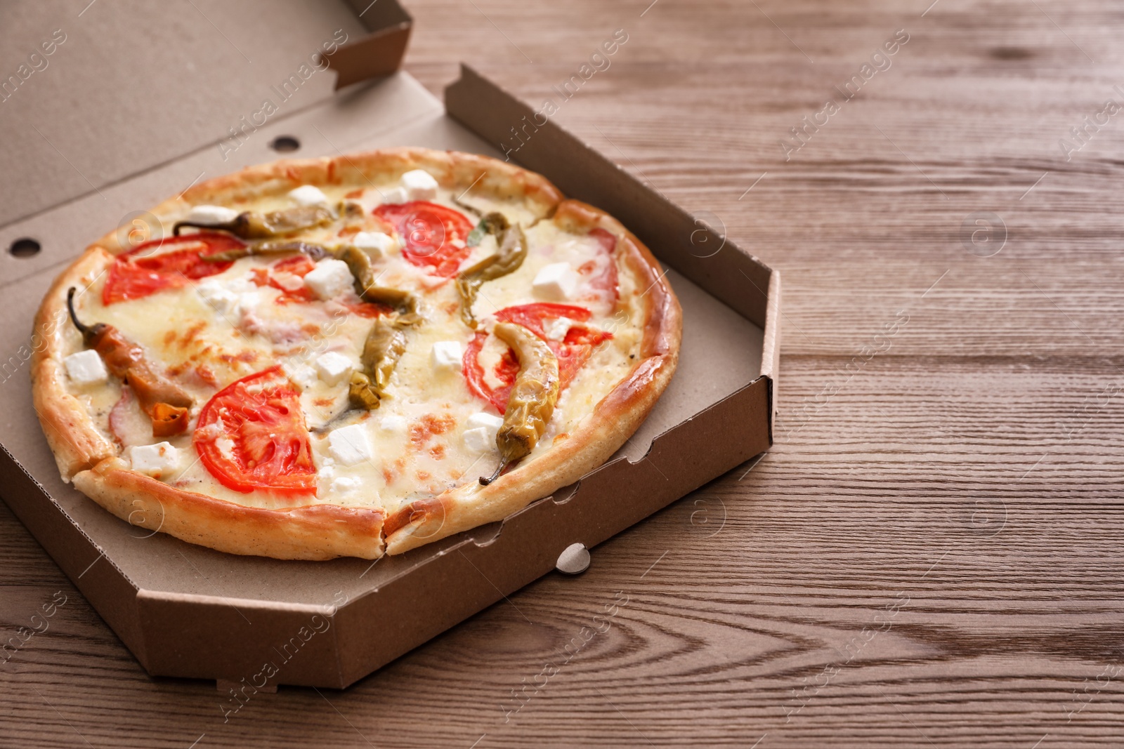 Photo of Cardboard box with tasty pizza on wooden table. Space for text