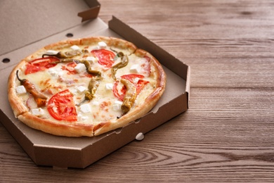 Cardboard box with tasty pizza on wooden table. Space for text