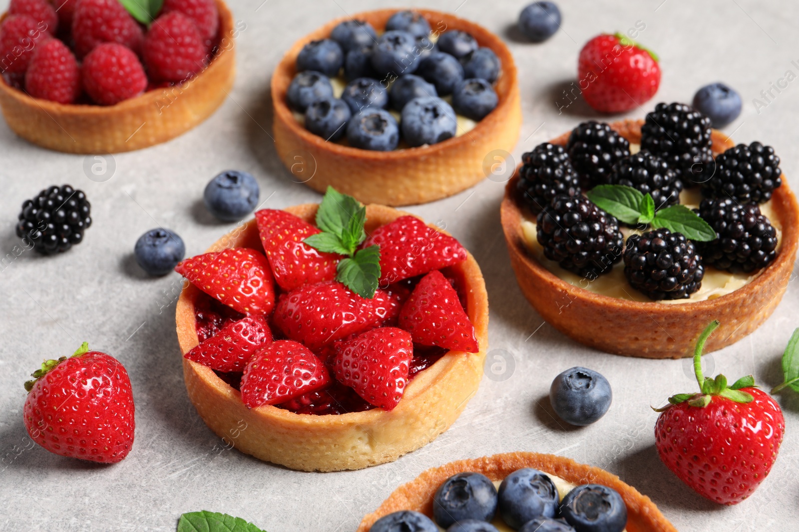 Photo of Tartlets with different fresh berries on light grey table. Delicious dessert