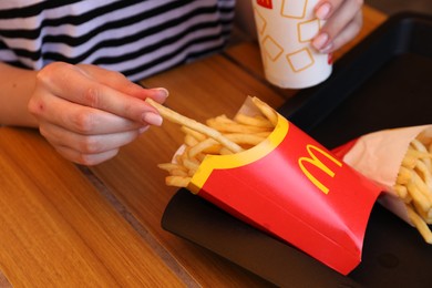 MYKOLAIV, UKRAINE - AUGUST 11, 2021: Woman with McDonald's French fries and drink at table in cafe, closeup